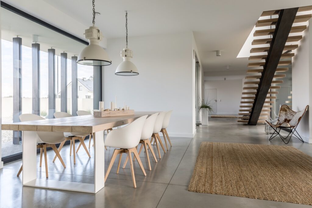 Moderne eethoek met houten tafel, witte stoelen en hanglampen naast een open trap en een jute vloerkleed